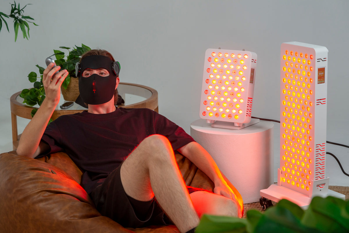 Man wearing the Ultra Laser Red Light Mask beside the Ultra Mini 100 and Ultra Pro 200 panels