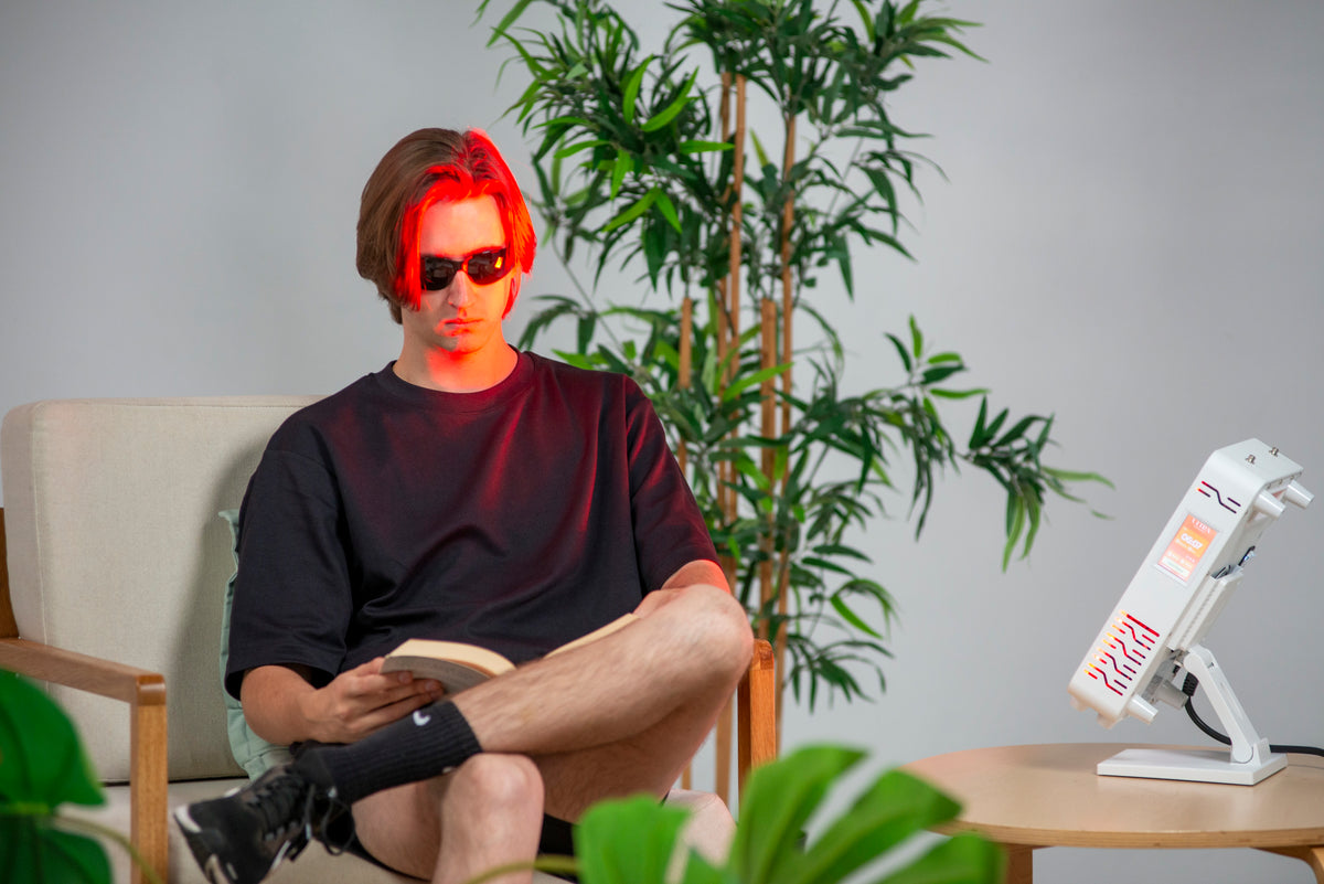 Man reading in an armchair beside the Ultra Mini 100 red light panel