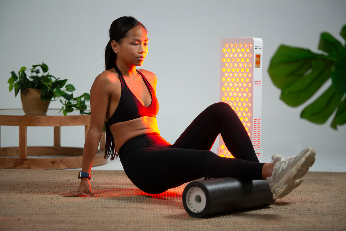 Woman using a foam roller beside the Ultra Pro 200 red light panel