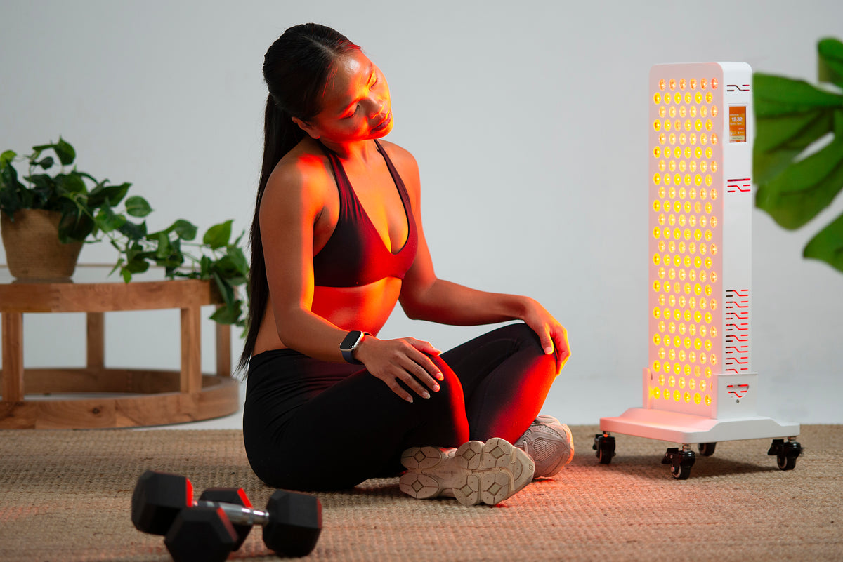 Woman seated on a mat beside the Ultra Pro 200 red light panel on the optional wheeled floor stand